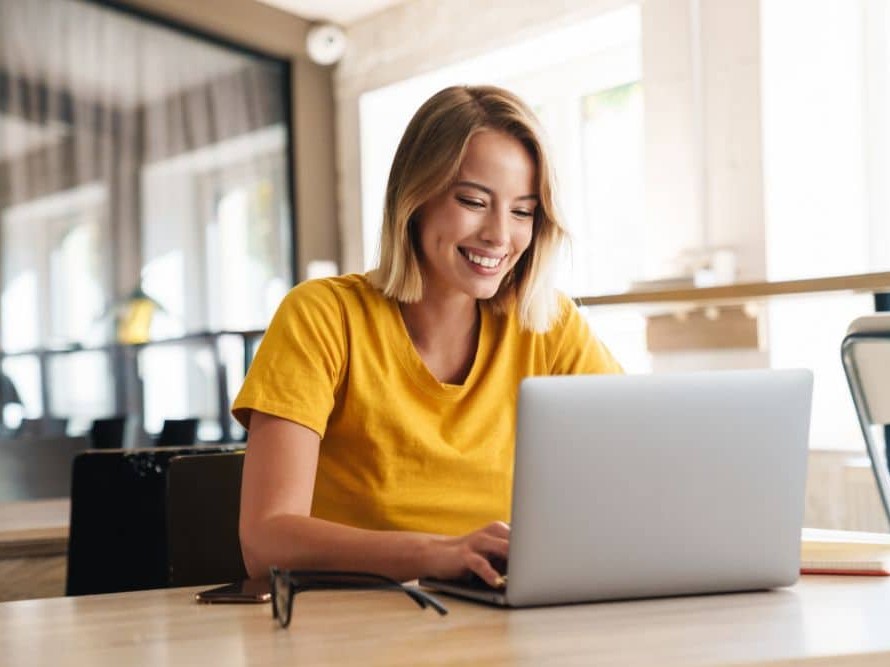 woman in yellow shirt working at computer smiling with teeth