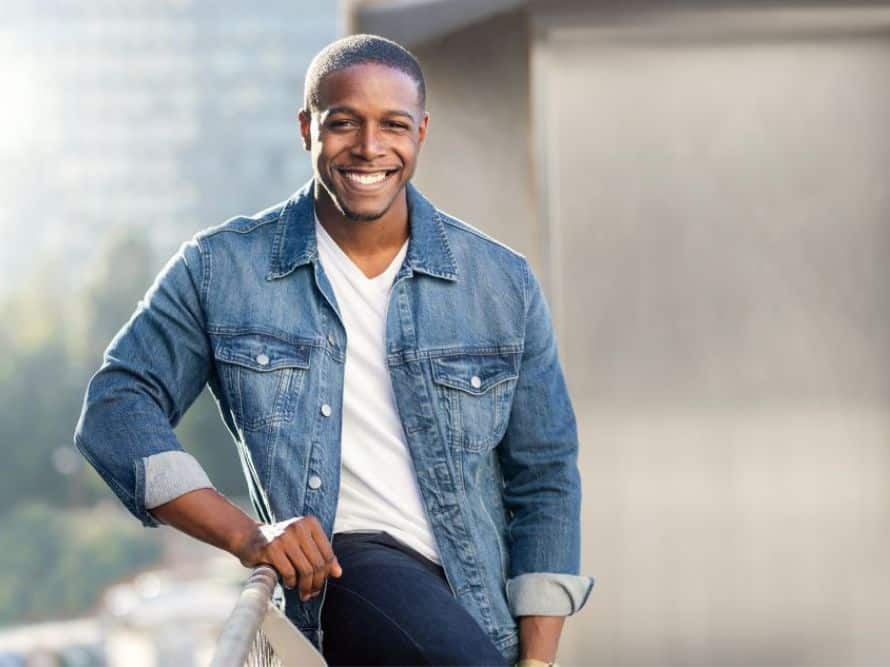Man wearing denim shirt leaning against rail smiling