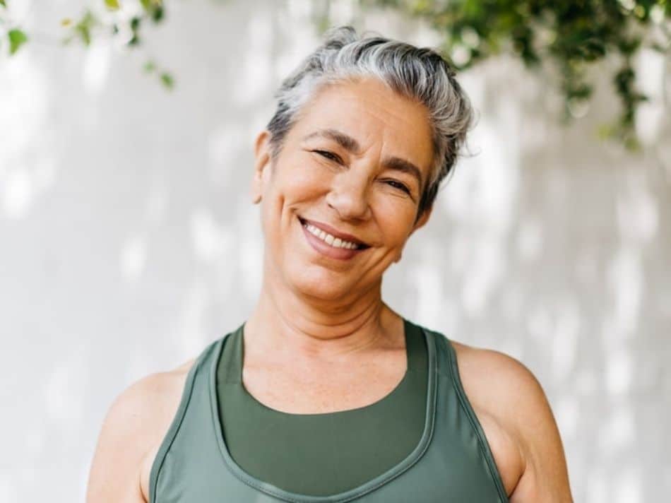 A middle-aged woman standing outside wearing a green sleeveless shirt smiling
